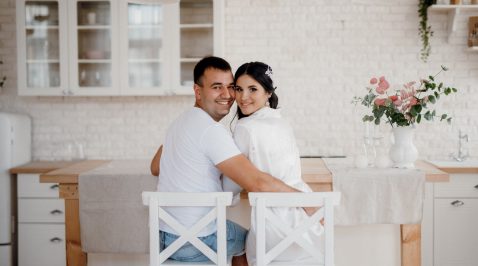 Casal feliz em roupas brancas que remetem a casamento na cozinha da sua primeira casa